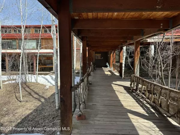 Covered wooden walkway beside a building, with rustic railings and patches of snow.