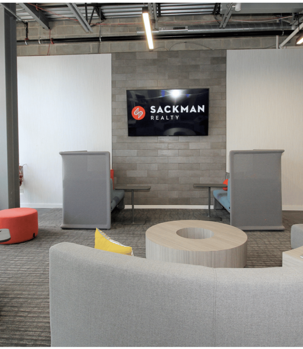 Office lounge with a Sackman Realty sign on a gray stone-tile wall.