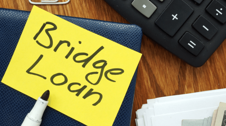 A yellow “Bridge Loan” note on a blue notebook beside a calculator and papers.