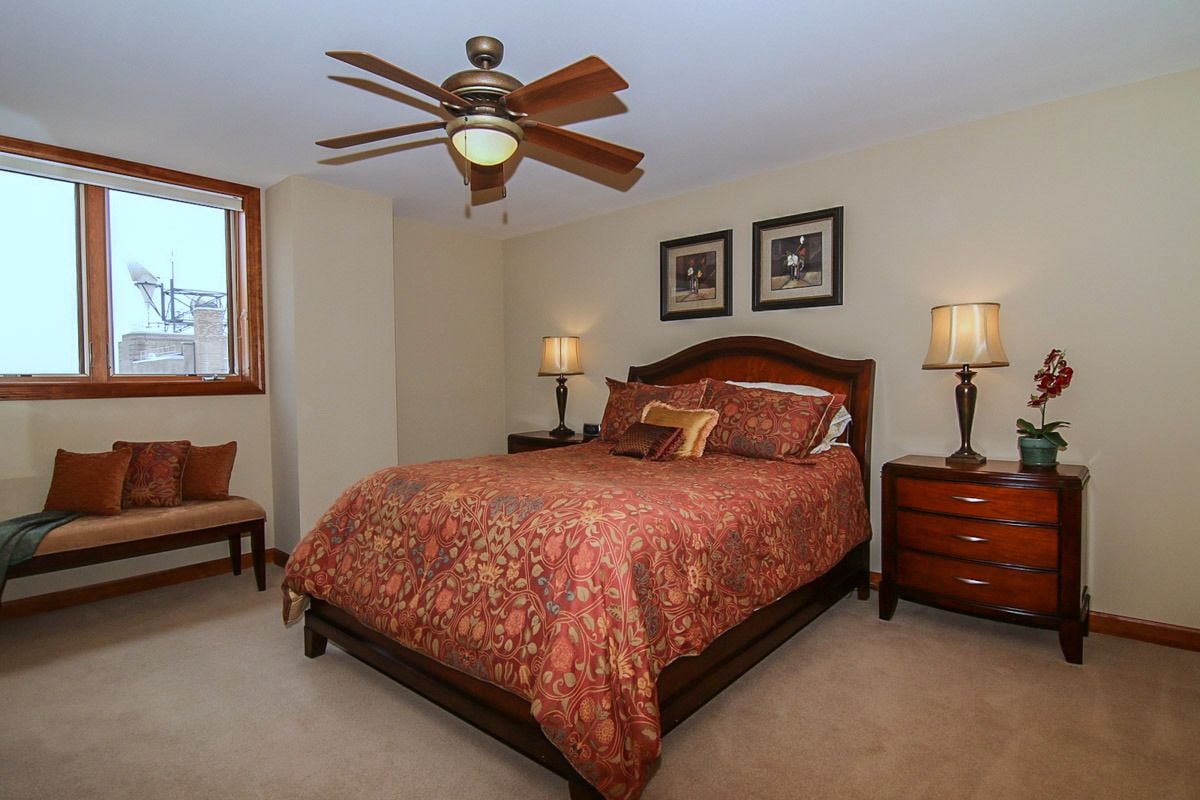 Penthouse bedroom with red patterned bedding, dark wood furniture, and a bench beside the window.