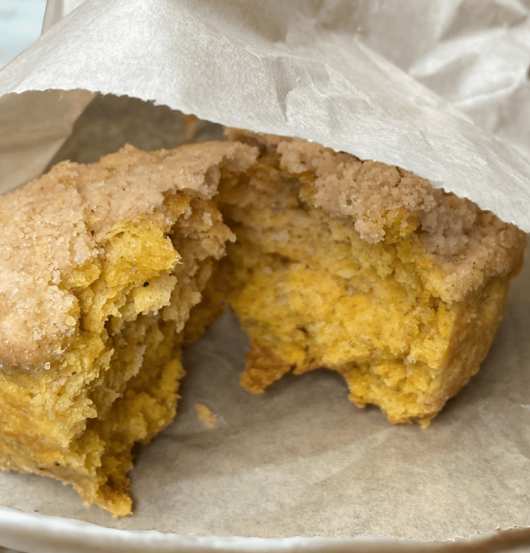 A close-up shot of a scone with a crumb topping broken open to reveal its interior texture, which is soft and moist.