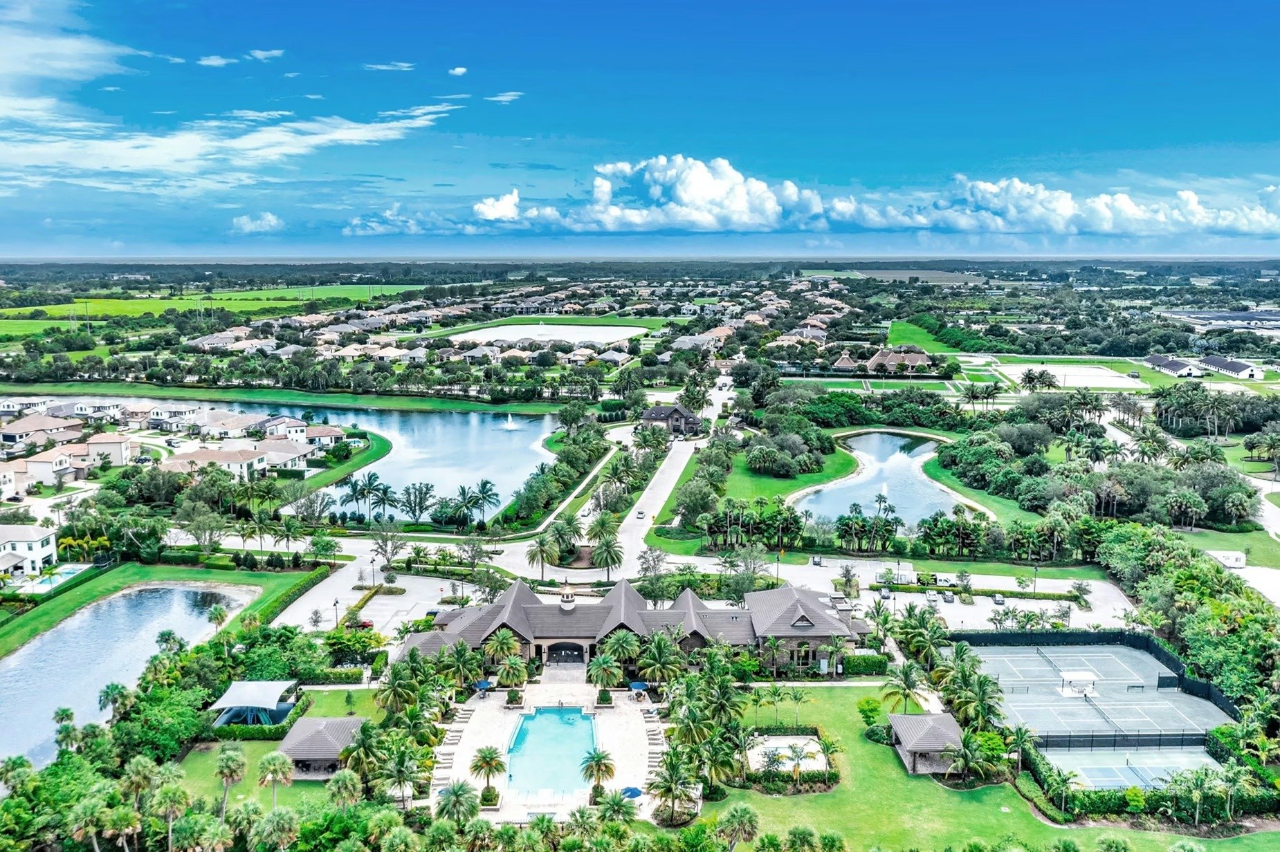Aerial view of a residential community, with a large estate, pool, tennis courts, and ponds in the foreground.