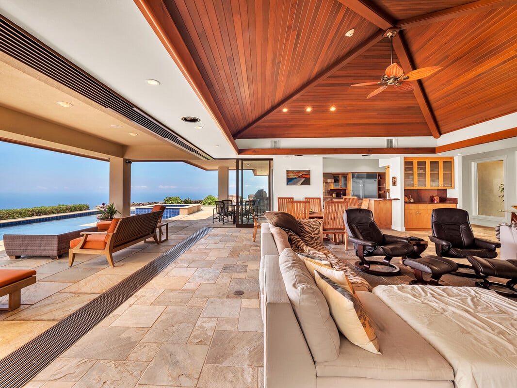 Ocean-facing living room with vaulted wood ceiling, opening to a pool terrace.