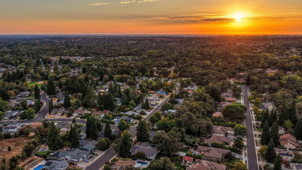 Aerial view of a tree-filled suburban neighborhood beneath a vivid sunset.