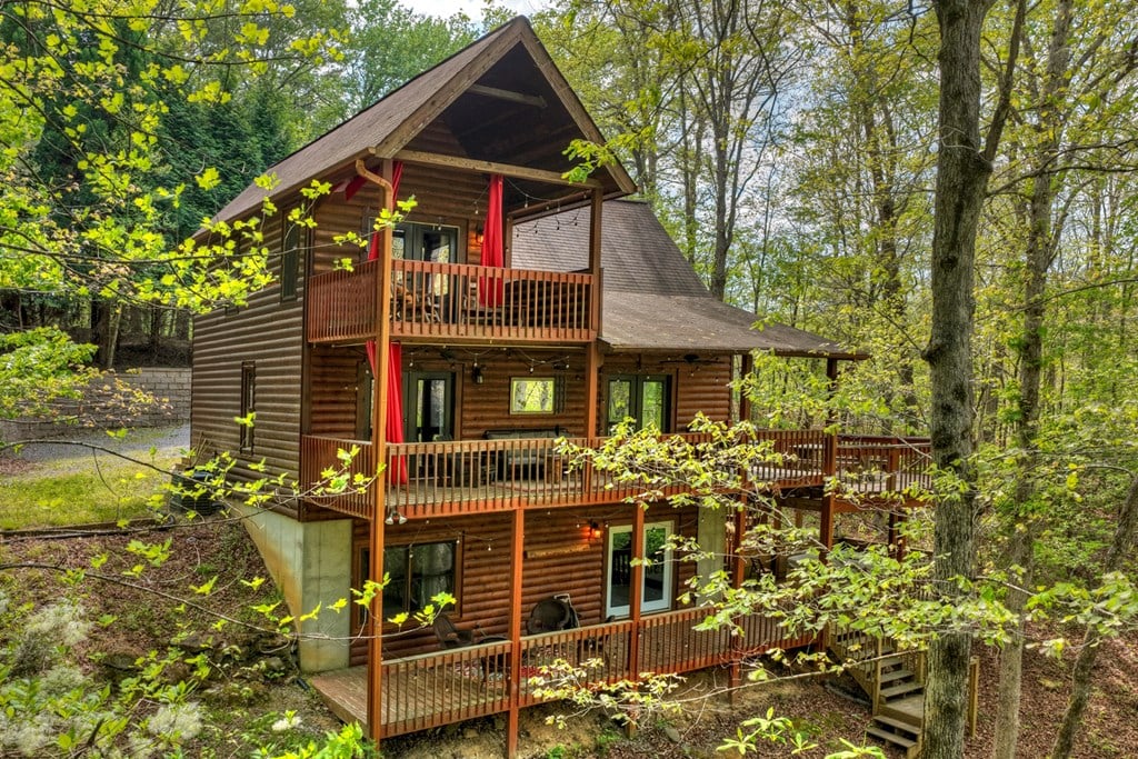 Multi-level log-sided mountain home with broad wooden decks and red support posts among trees.