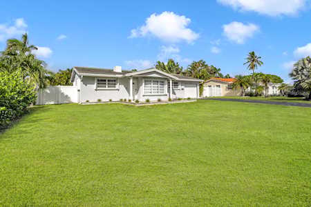 Single-story white house beyond a broad lawn, framed by tropical landscaping and palm trees.