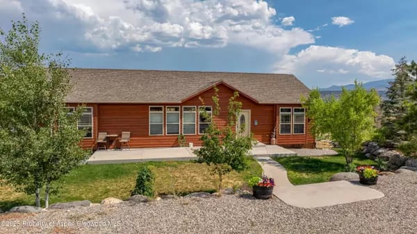 Red-brown single-story house with a curved front walkway, landscaped yard, and distant mountains.