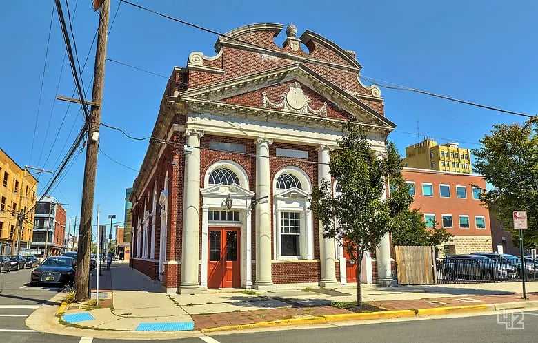 Red-brick street-corner building with ornate columns, arched windows, and red entrance doors.