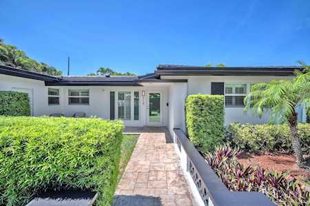 Single-story home with a paved entry walkway, trimmed hedges, and tropical landscaping.