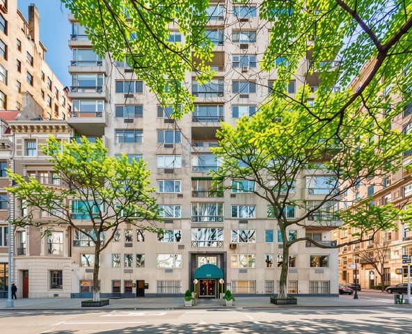 Multi-story apartment building behind leafy sidewalk trees, with a central entrance facing the street.