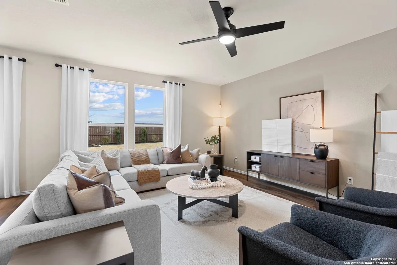 Staged living room with a gray sectional, round coffee table, and windows overlooking a fenced yard.