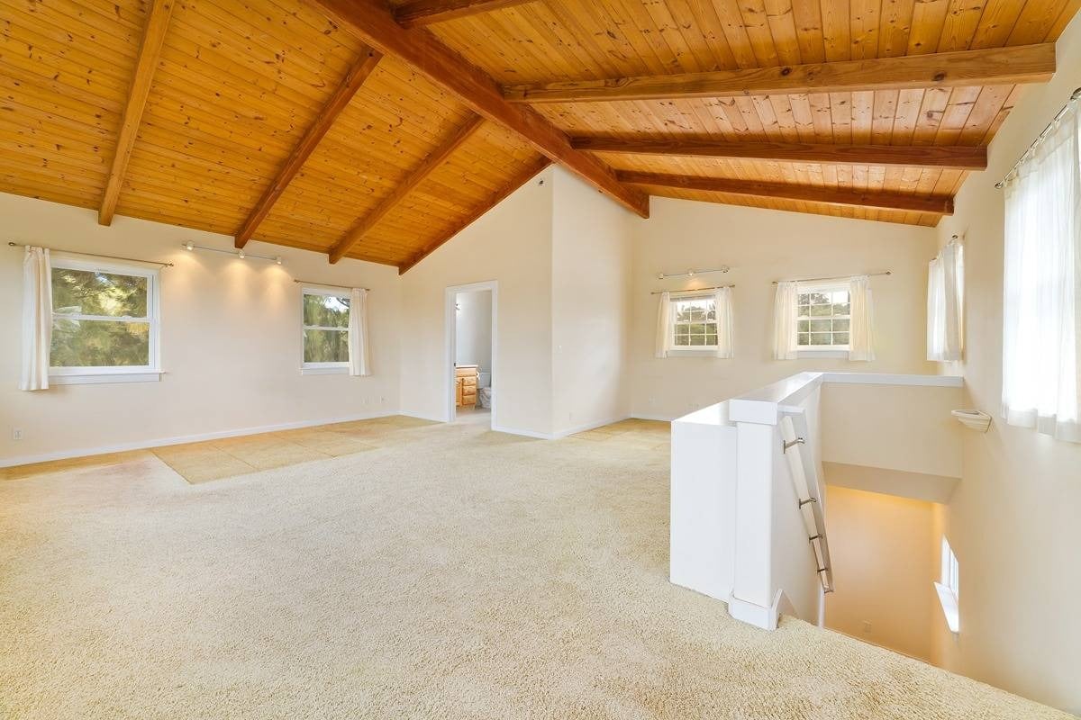 Vacant loft with a vaulted wood-plank ceiling, exposed beams, and an open stairwell.