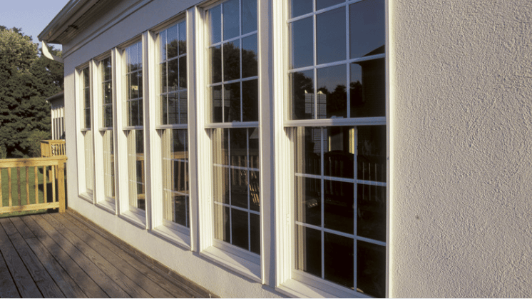 House facade with tall multi-pane windows beside a weathered wooden deck and railing.