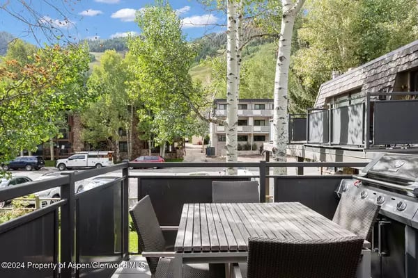 Outdoor patio with a dining table and grill overlooking leafy trees and a wooded hillside.