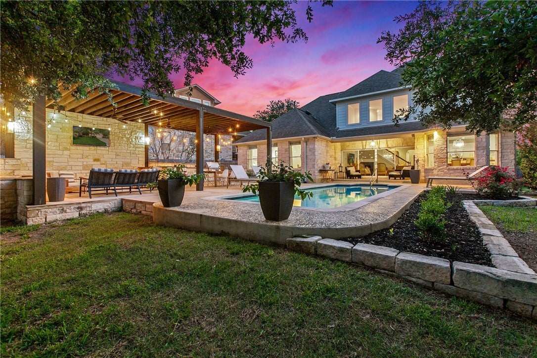 Stone home with an illuminated covered patio and swimming pool at sunset.