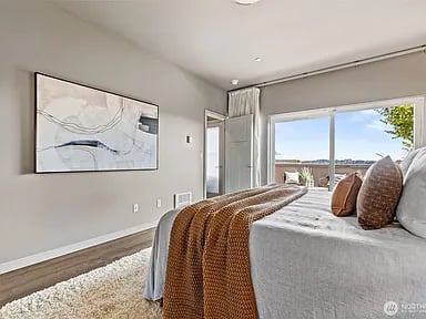 Staged bedroom with a rust-colored throw and sliding glass doors opening to a balcony.