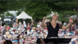 A woman conducts music onstage before a crowd at an outdoor festival.