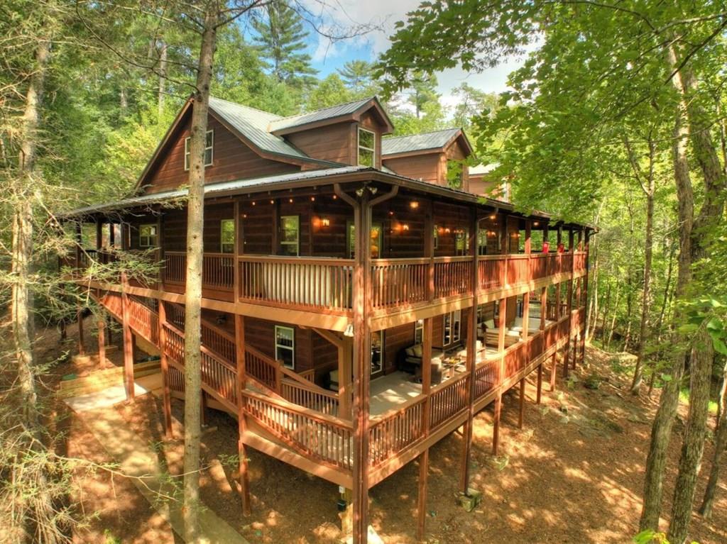 Wooded cabin with a metal roof, illuminated screened porch, and expansive multi-level decks.