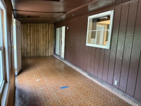 Empty enclosed porch with brown paneling, patterned tile floor, and a window into an adjoining room.