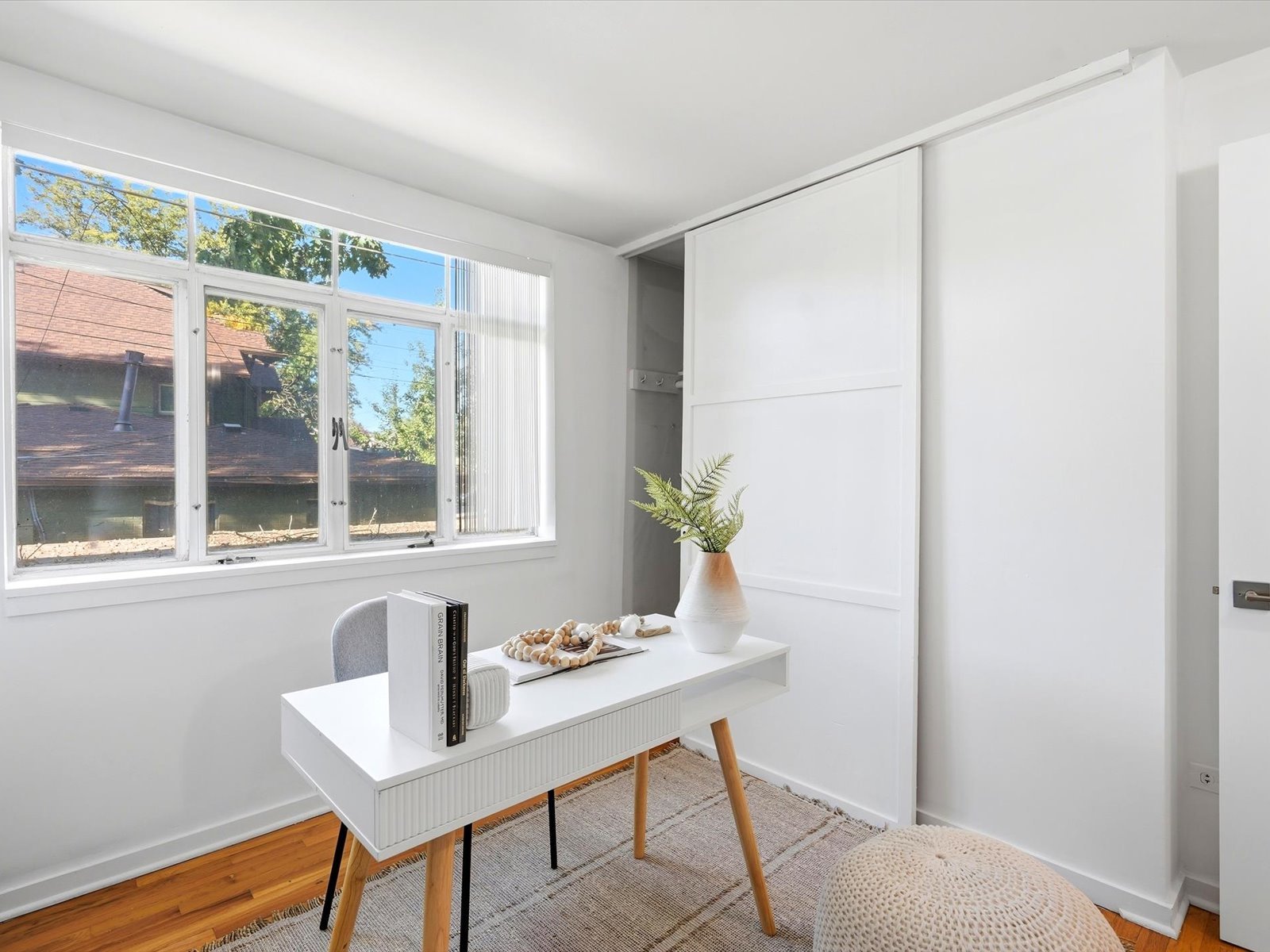 Bright home office with a white desk beside a large window and sliding closet door.