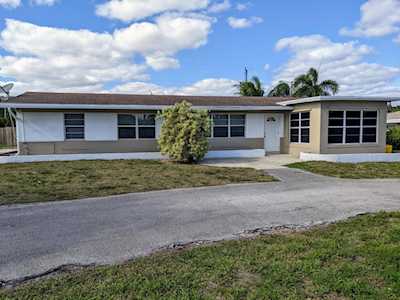 Single-story ranch home with broad front windows, a paved driveway, and palm trees behind it.