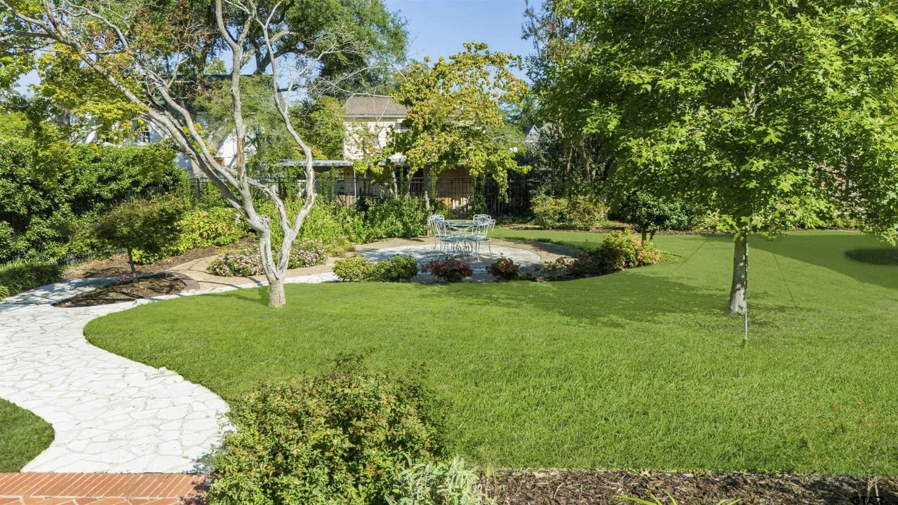outdoor garden area with white stones and circular english style patio funriture (table and chairs) wirh green grass and small flowers surrounding patio