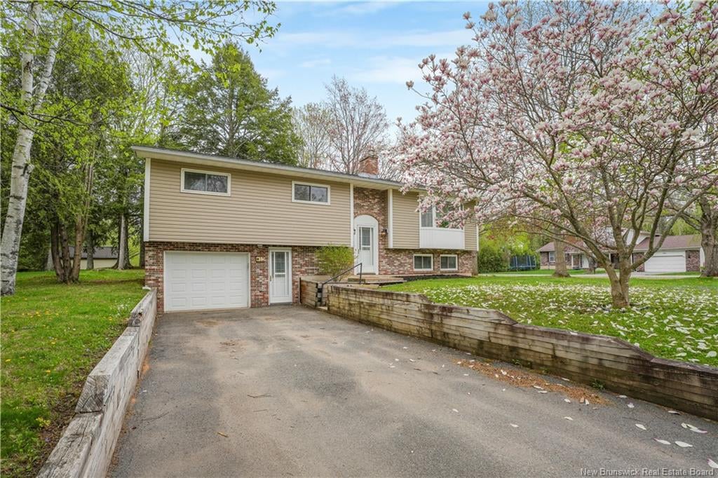 Split-level home with brick lower story, paved driveway, and pink-flowering tree in the front yard.