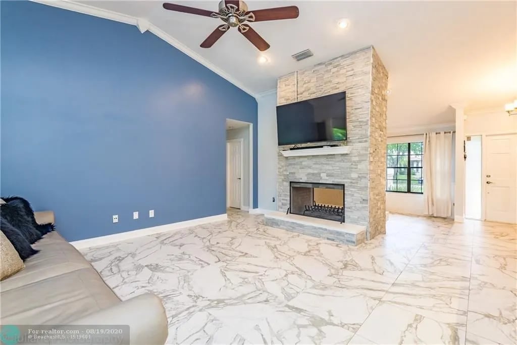 Living room with a stone fireplace, mounted television, blue accent wall, and marble-look tile floor.
