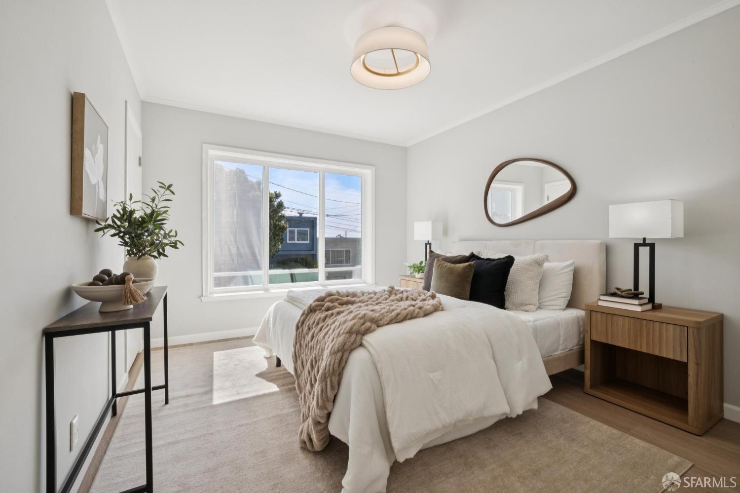 Staged bedroom with a white bed, neutral bedding, and an oval mirror above the headboard.