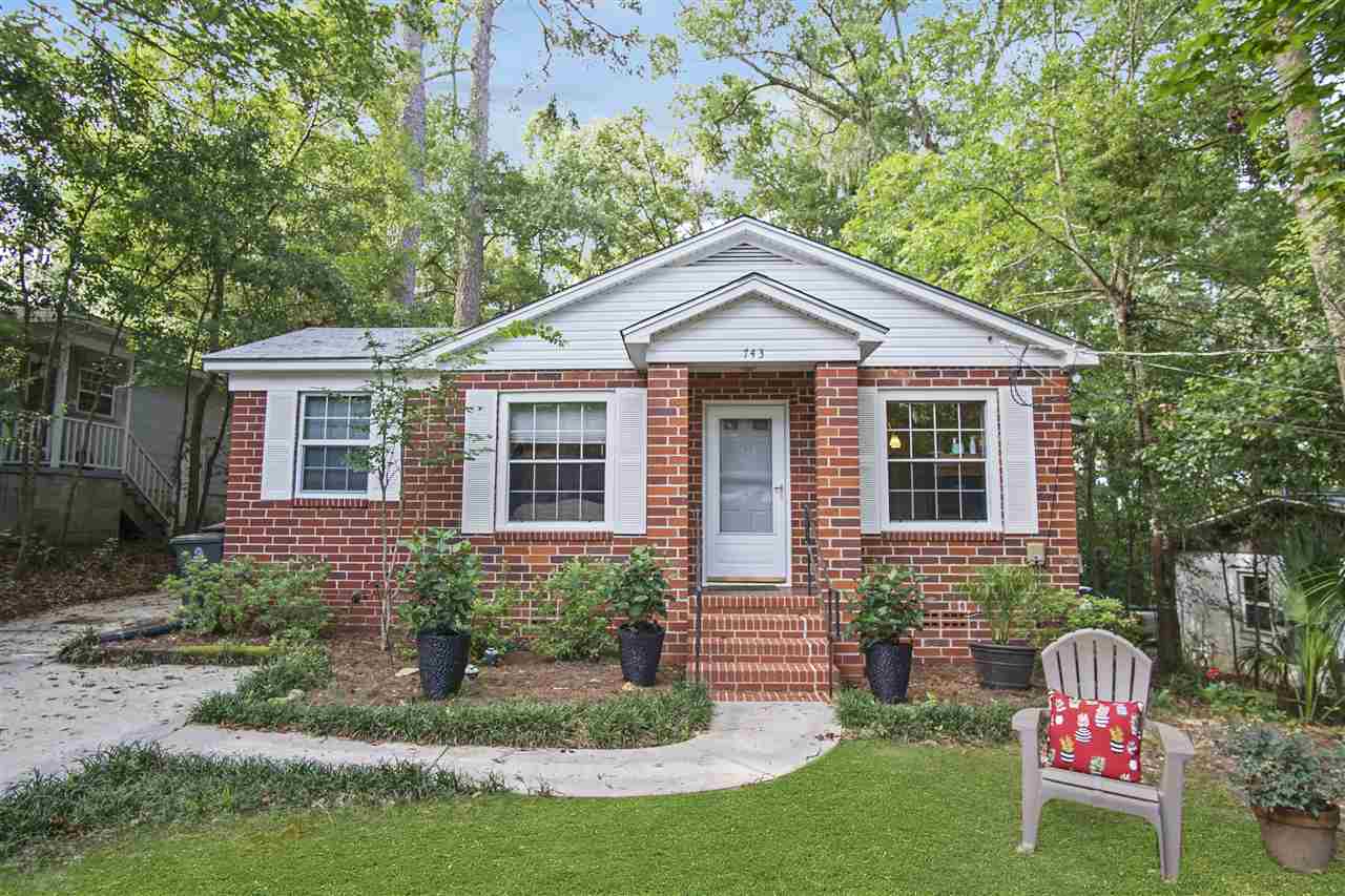 A small brick house surrounded by a green lawn and trees, showcasing a serene and inviting outdoor environment.