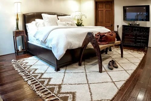 Bedroom with white bedding, a leather bag on a bench, and a patterned rug.