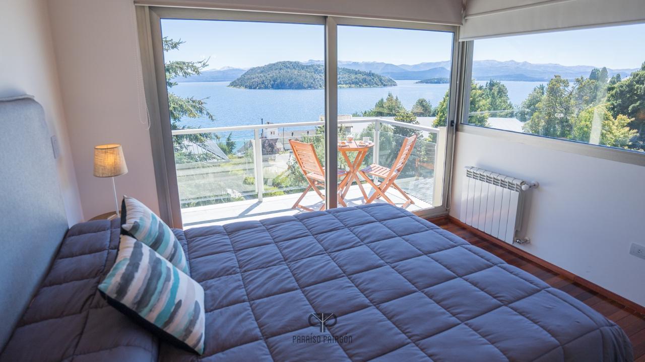 Bedroom with a large bed facing glass doors and a balcony overlooking a lake.