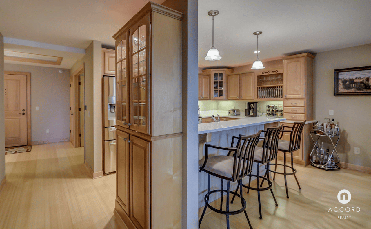 Condo kitchen with a long breakfast bar, stools, and light-wood cabinetry beside the entry hall.