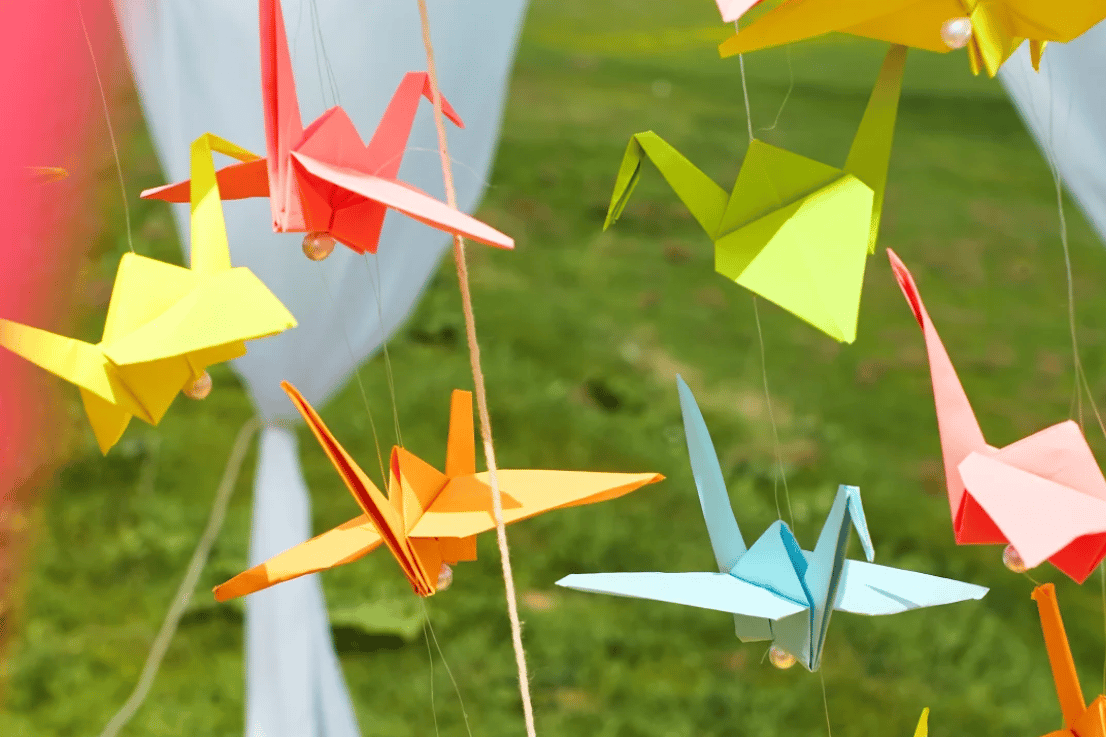 Colorful origami cranes hang on strings against a soft-focus green background.