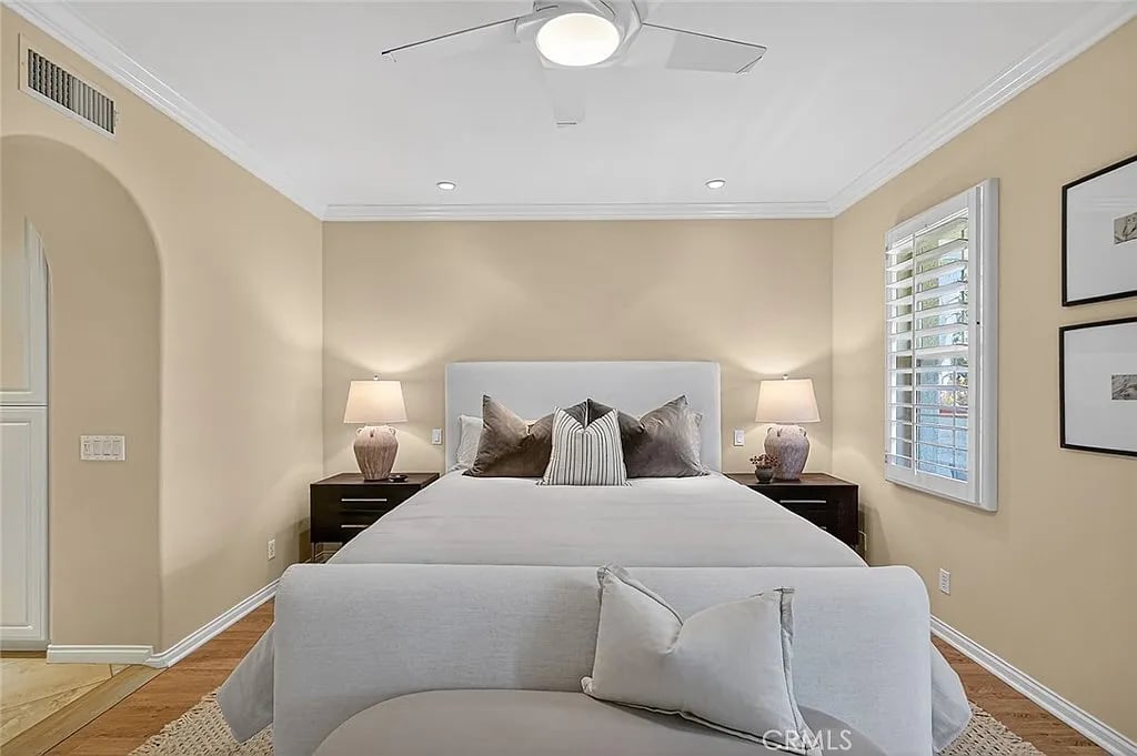 Bedroom with a large bed, upholstered bench, matching nightstands, and a shuttered window.