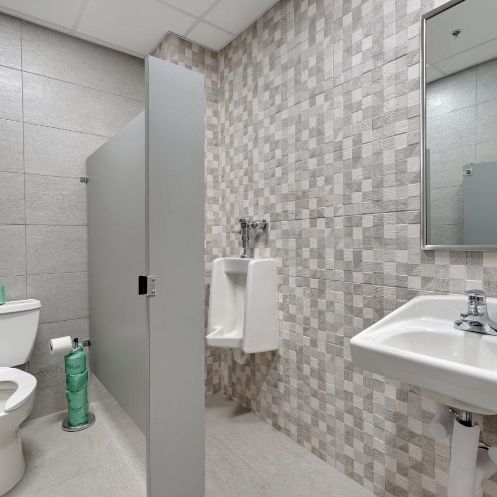 Tiled restroom with a gray toilet partition, wall-mounted urinal, and white sink.