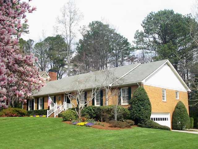 Brick ranch home with a white porch, green lawn, and blooming magnolia trees.
