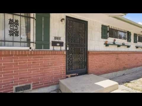 Home exterior with red brick lower facade, barred windows, and an ornate black security door.
