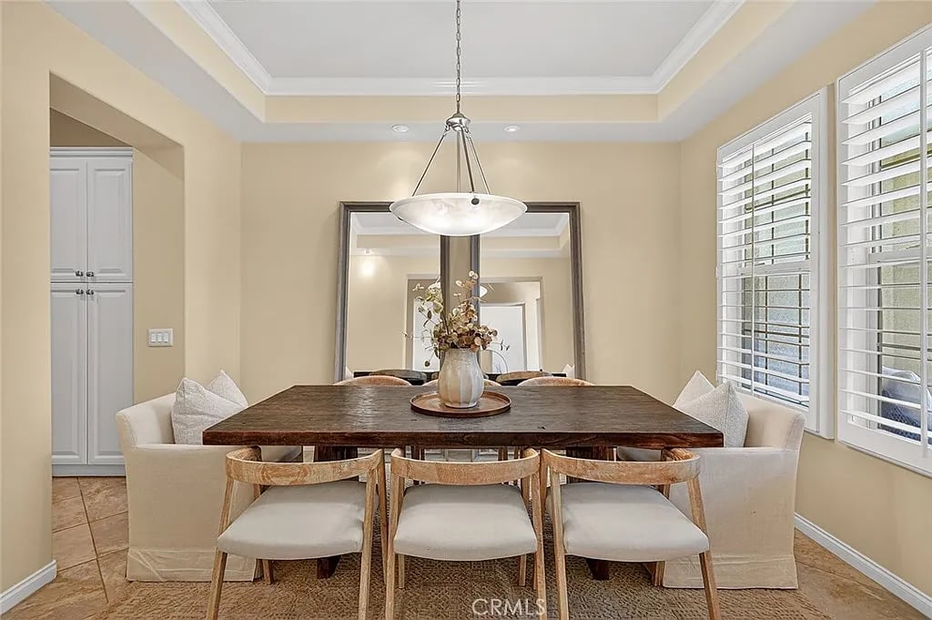 Staged dining room with a dark wood table, upholstered chairs, and plantation shutters.