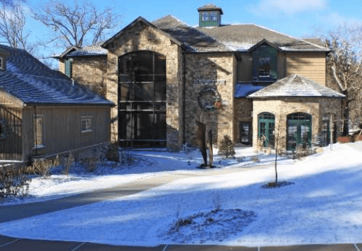 Stone-and-wood building with a tall central window and snowy grounds.