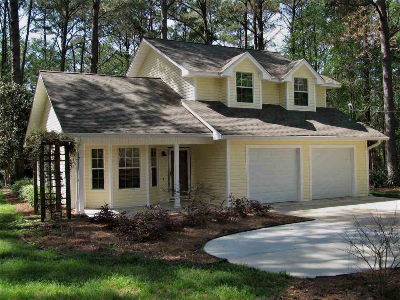 A yellow house featuring a garage and a driveway, set against a clear sky.