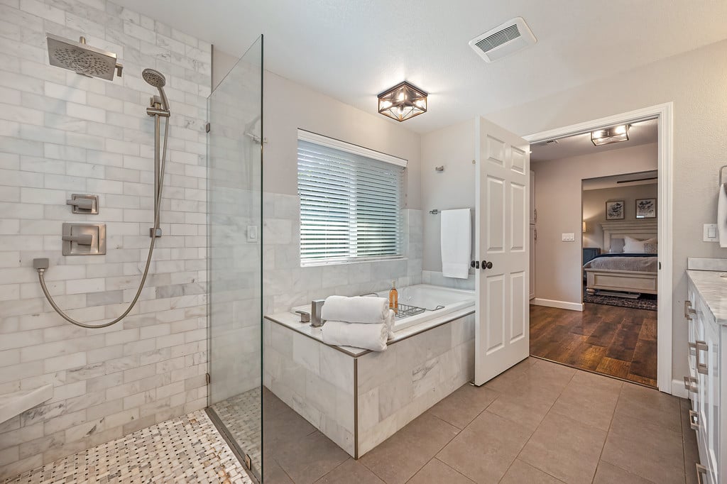 Primary bathroom with marble-tile shower and soaking tub beside a bedroom doorway.