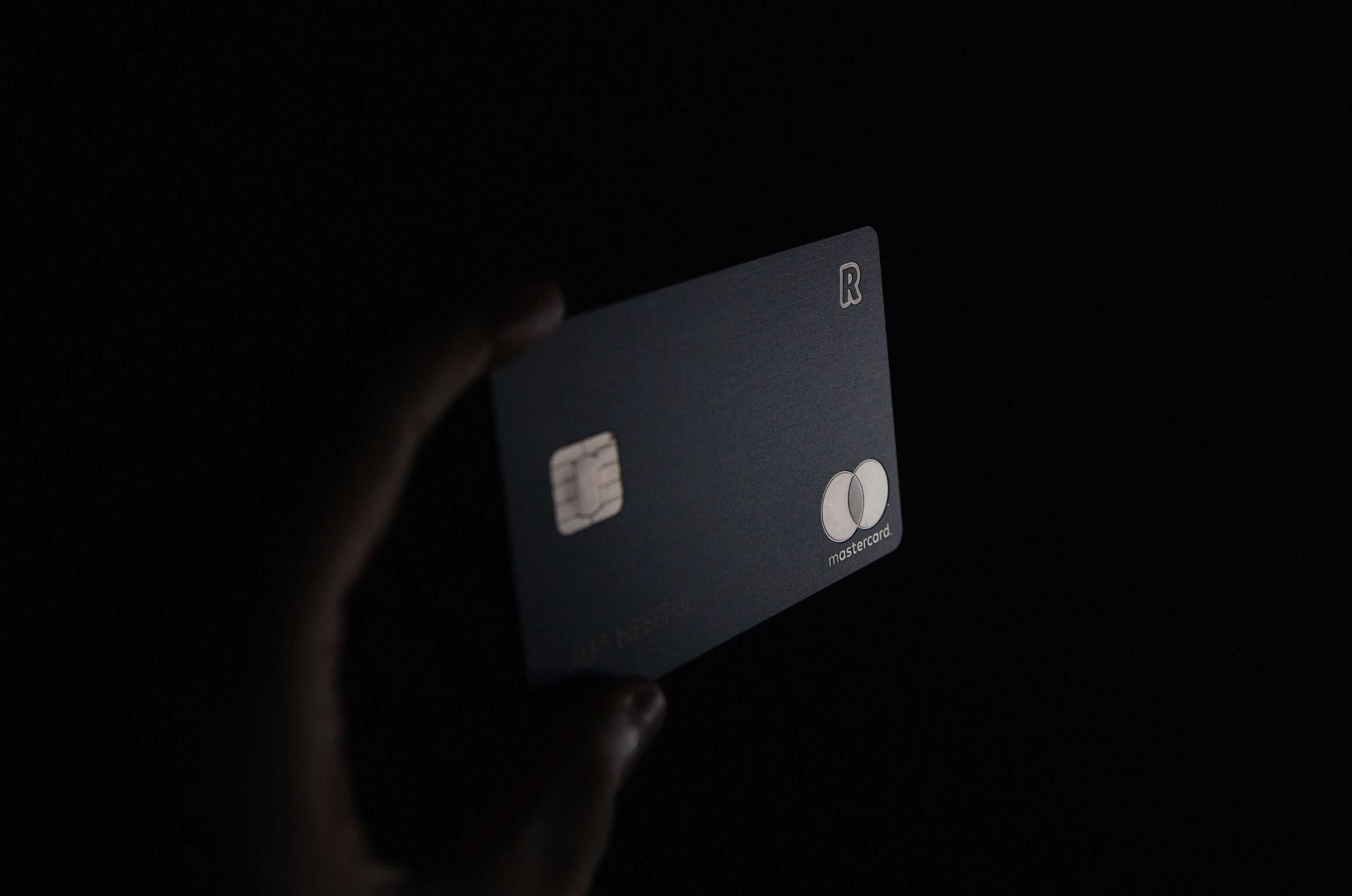 A hand holds a dark Mastercard credit card with a visible chip.
