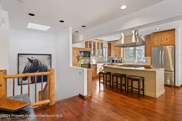 Kitchen with wood cabinetry, stainless steel appliances, and a large island with bar stools.