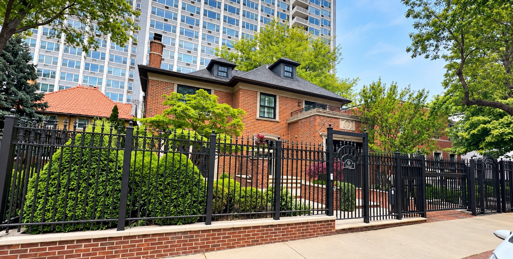 Brick single-family home behind a wrought iron fence with a lakefront high-rise in Buena Park, Chicago