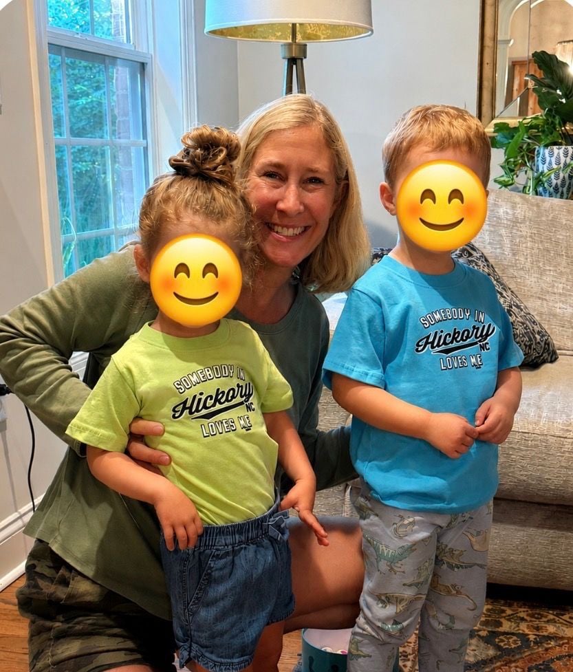 A smiling woman kneels beside two children wearing Hickory-themed shirts.