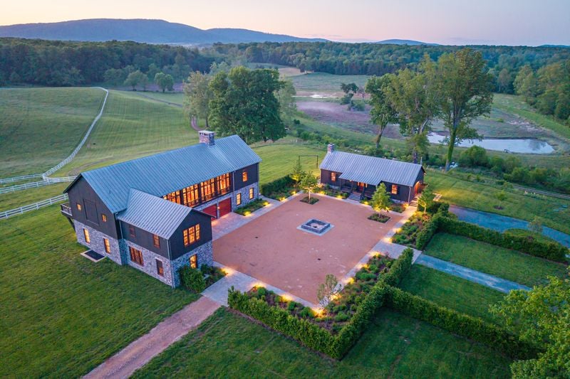 Aerial view of a rural estate with stone buildings, a courtyard, fields, and distant mountains.