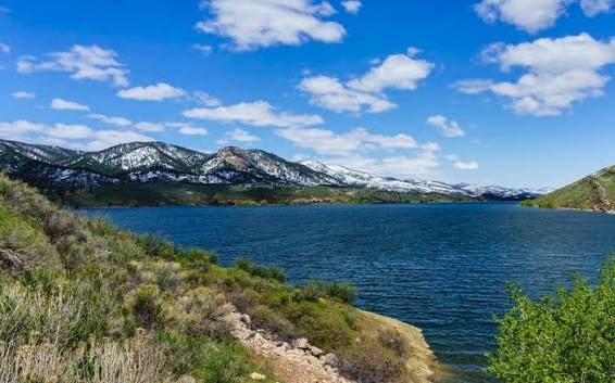 Blue lake and rocky shore with snow-dusted mountains in the distance.