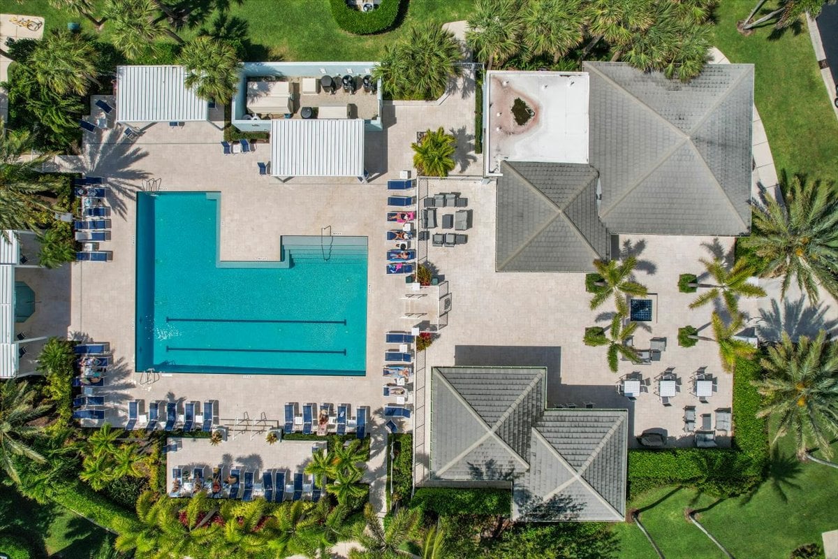 Aerial view of a condominium pool courtyard with palm trees, lounge chairs, and surrounding buildings.