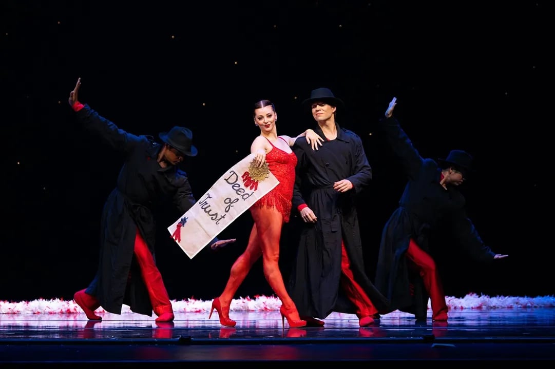 Dancers performing a theatrical, jazzy number during Smuin Contemporary Ballet's The Christmas Ballet in San Francisco, featuring a female dancer in red holding a 'Deed of Trust' prop.